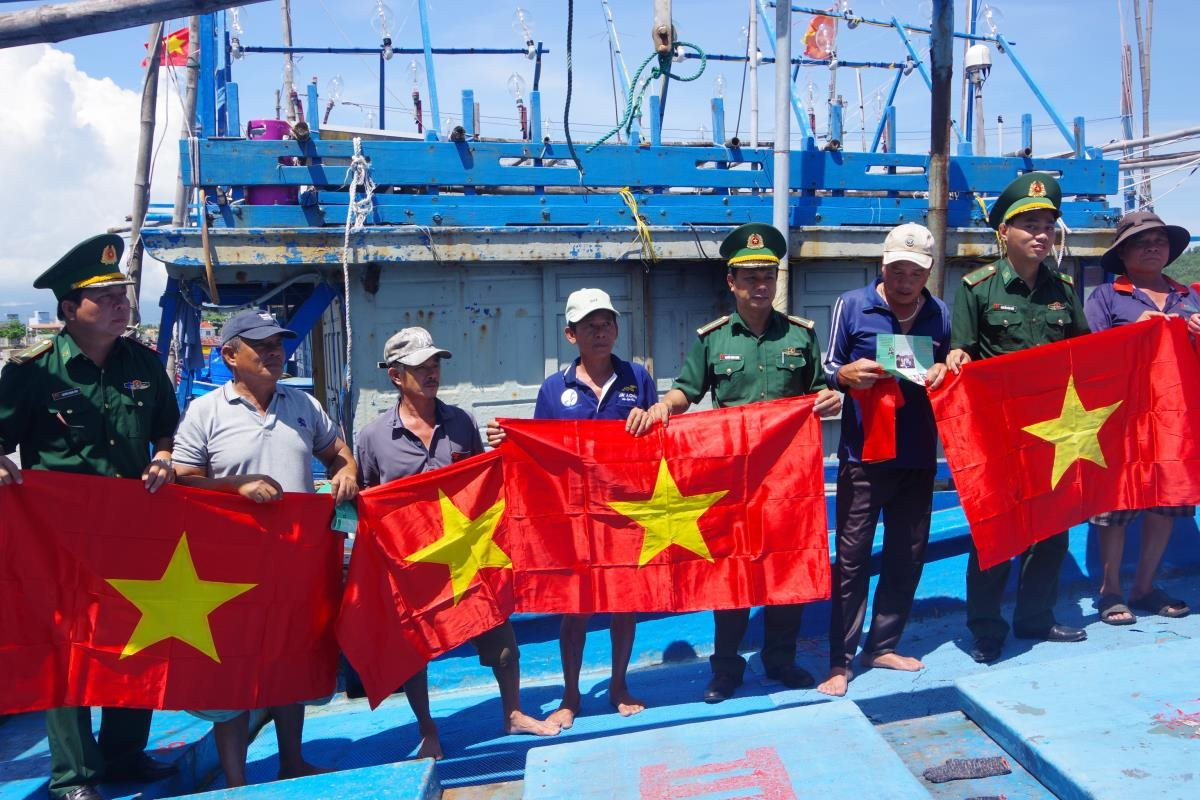 Cán bộ BĐBP Bình Định tuyên truyền chống khai thác IUU và tặng cờ Tổ quốc cho ngư dân vươn khơi bám biển. Ảnh: Công Cường.