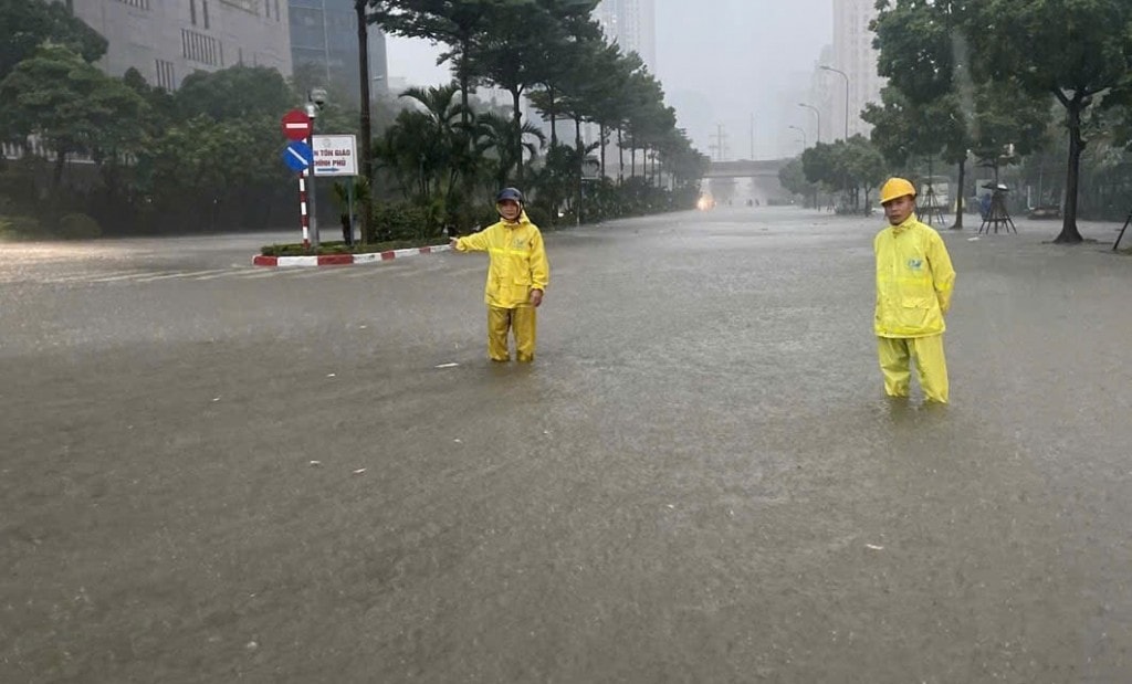 Công nhân Xí nghiệp Thoát nước số 2 ứng trực kết hợp phân luồng giao thông tại điểm ngập trên phố Dương Đình Nghệ. Ảnh: Ngọc Uyên