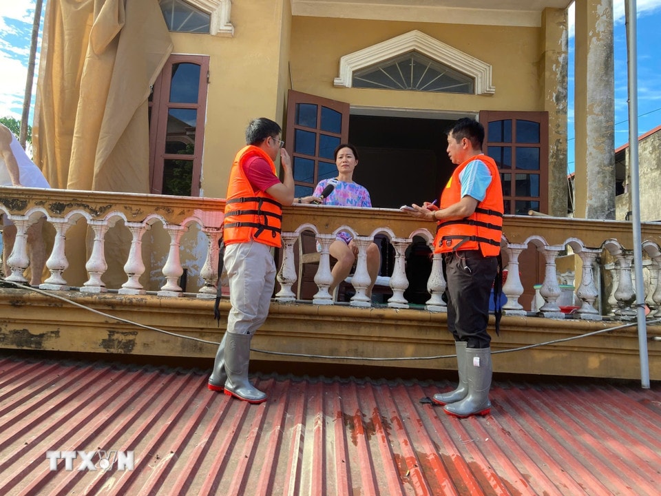 Phóng viên TTXVN đứng trên mái nhà phỏng vấn người dân về tình hình ứng phó với ngập lụt. (Ảnh: Thắng Trung/TTXVN)