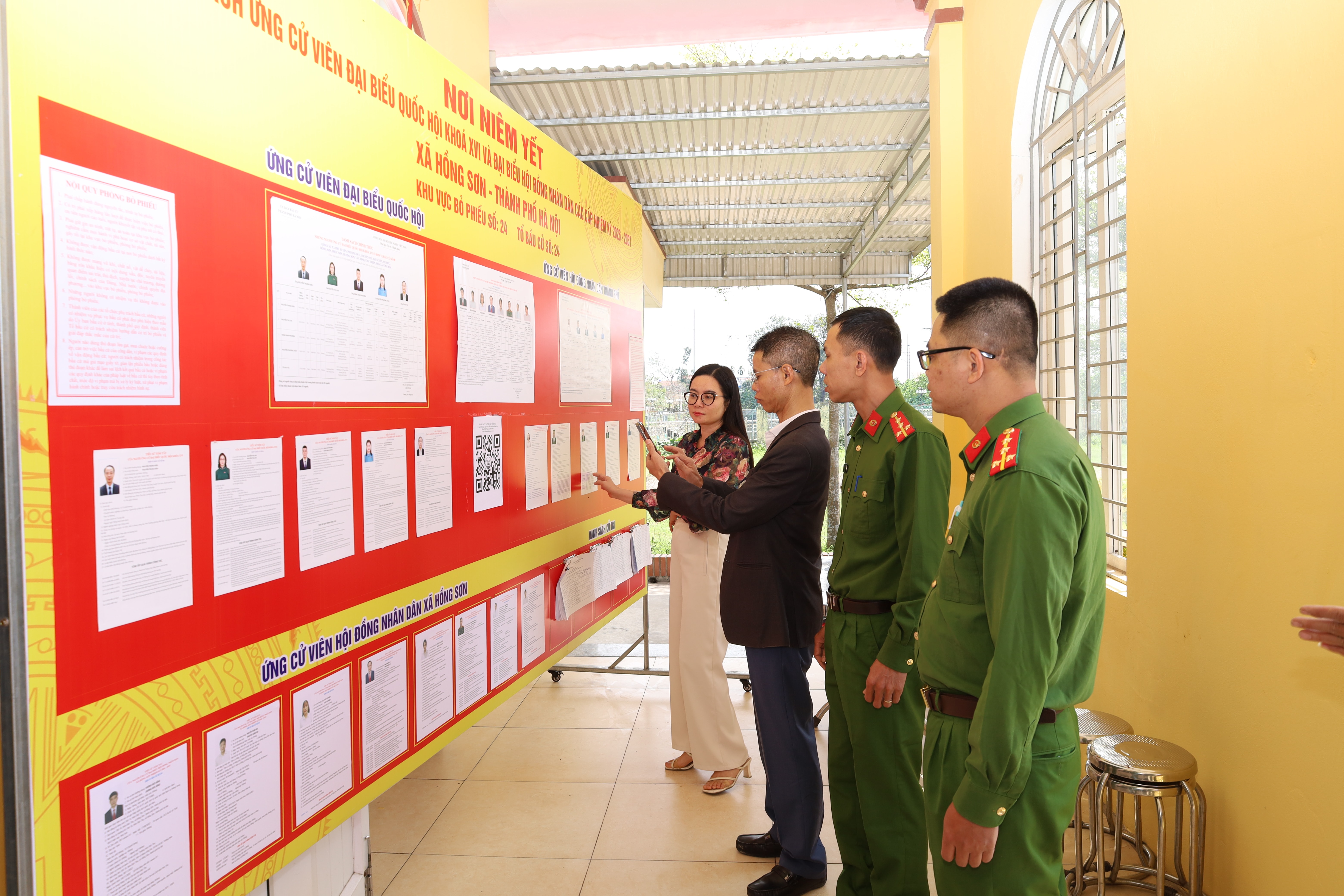 Chủ tịch UBND xã Hồng Sơn Ngô Quốc Ca kiểm tra điểm niêm yết danh sách cử tri, ứng cử viên đại biểu Quốc hội, HĐND các cấp và hoạt động của mã QR tại khu vực bỏ phiếu. Ảnh: Kim Nhuệ