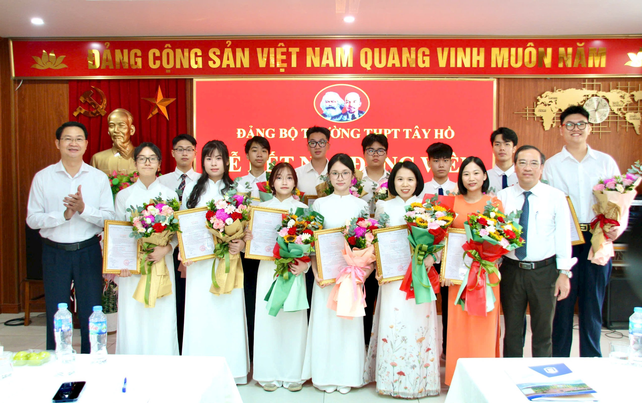 Đồng chí Trần Quang Đạo, Phó Bí thư Thường trực Đảng ủy phường Phú Thượng (bên phải) và đồng chí Nguyễn Anh Tuấn, Bí thư Đảng ủy, Hiệu trưởng Trường THPT Tây Hồ (bên trái) trao quyết định kết nạp Đảng và tặng hoa cho các đảng viên mới. Ảnh: Hoàng Vũ