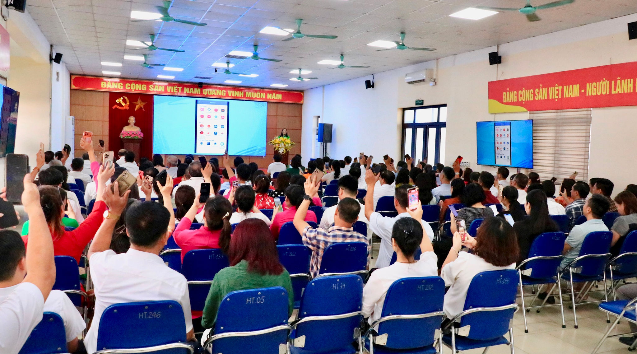 Tại hội nghị, các đại biểu, cán bộ và đảng viên phường Lĩnh Nam đã cùng thực hiện thao tác bằng điện thoại trên ứng dụng iHanoi để tham gia Cuộc thi. Ảnh: LN