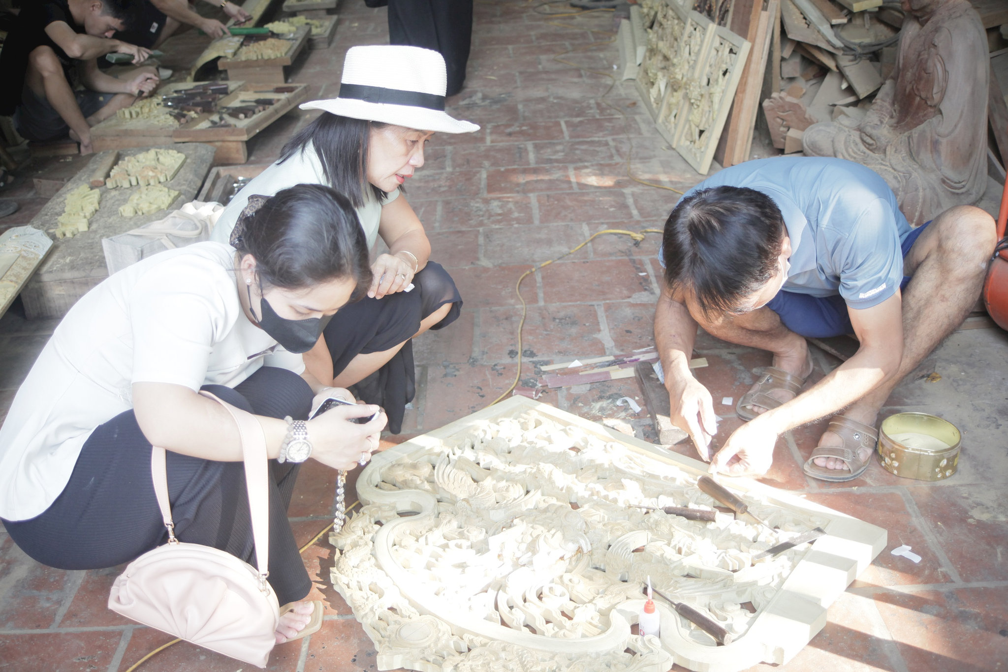 Du khách tìm hiểu kỹ thuật chạm khắc gỗ truyền thống tại một cơ sở sản xuất ở làng nghề Sơn Đồng. Ảnh: PV